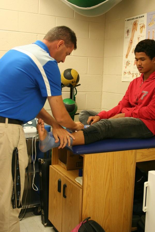 Another athletic trainer Mr. Gregory wraps Piyasak Pharaweks, senior, ankle because of a previous soccer injury he has sustained.  The pressure from the tape will hold the muscles together and support his ankle throughout the season, preventing a more major injury.