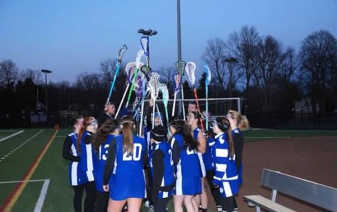 Junior Varsity girl’s lacrosse team embraces each other with their sticks held high