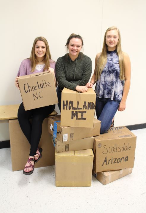 (left to right) Sarah Blase, Vada Murray, and Brianna Reitsch hold moving boxes with their new destination written on them. Those seniors will be moving the summer after graduation.