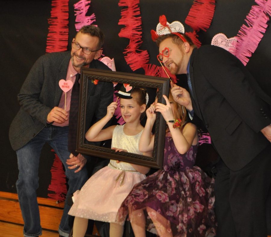 Fathers and daughters play dress up at the photo booth. This shows one of the activities at the dance, the photo booth. Families can dress up and take a silly photo by professional photographers.