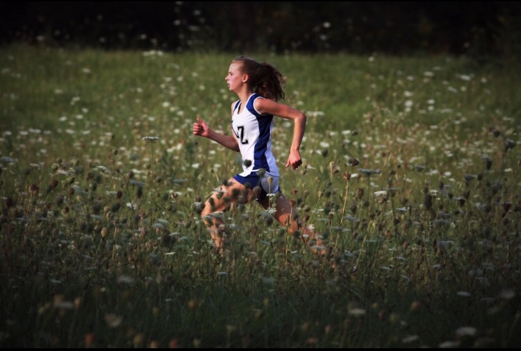 Hayley Burk, sophomore, runs through a field during a cross country meet. Burk attended the NSC leadership conference where they spoke about the new Hate Speech Protocol being implemented into LZHS's athletic program starting this fall.