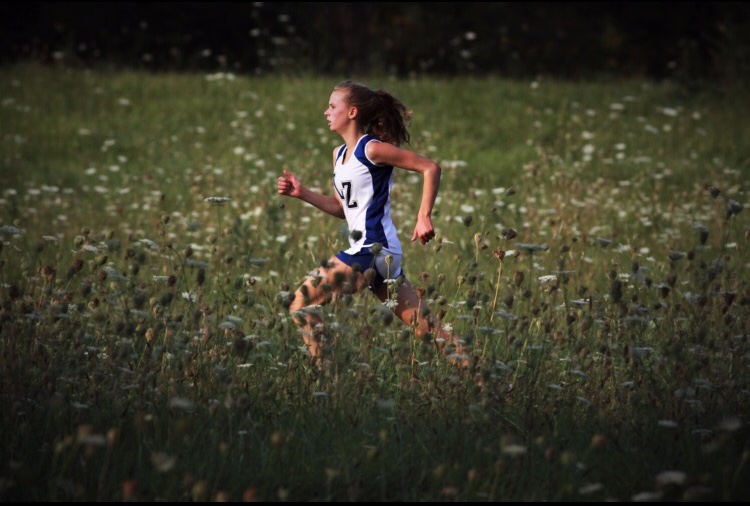 Hayley Burk, sophomore, runs through a field during a cross country meet. Burk attended the NSC leadership conference where they spoke about the new Hate Speech Protocol being implemented into LZHSs athletic program starting this fall.