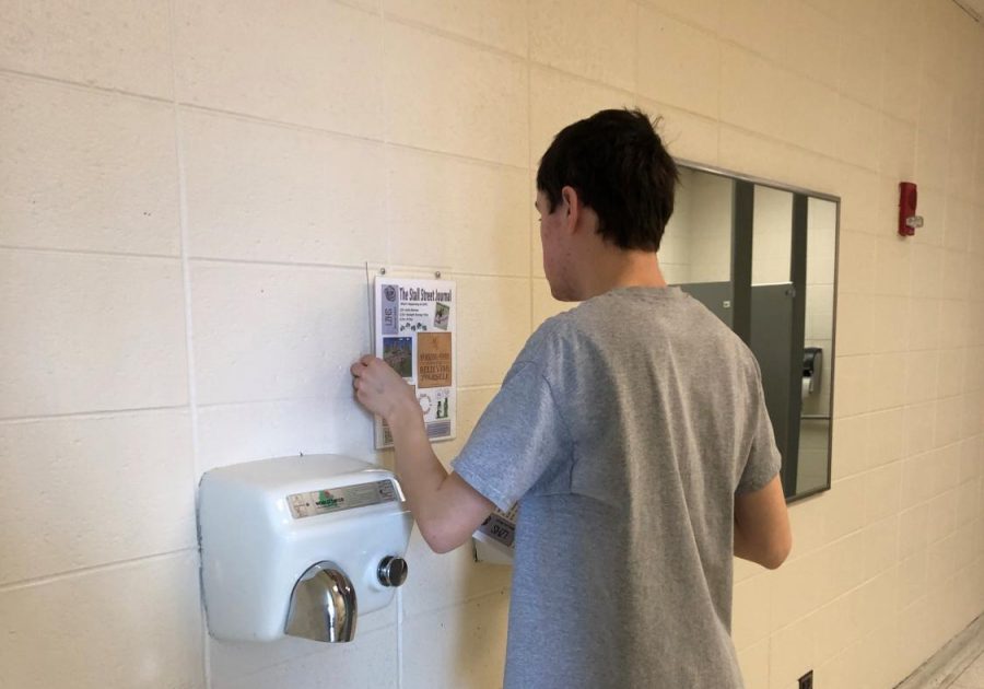 Andrew Koppel, transition student, posts a Stall Street Journal above the hand dryers. The students usually post the stall streets near the sinks as well as the stalls to promote good hygiene.