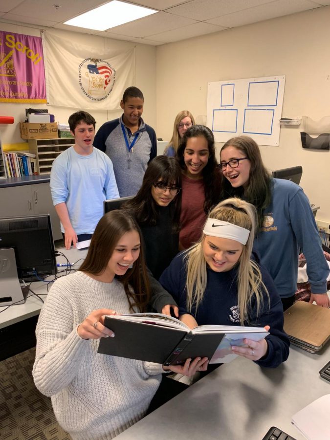 The yearbook staff huddles around a previous yearbook during their late night. 