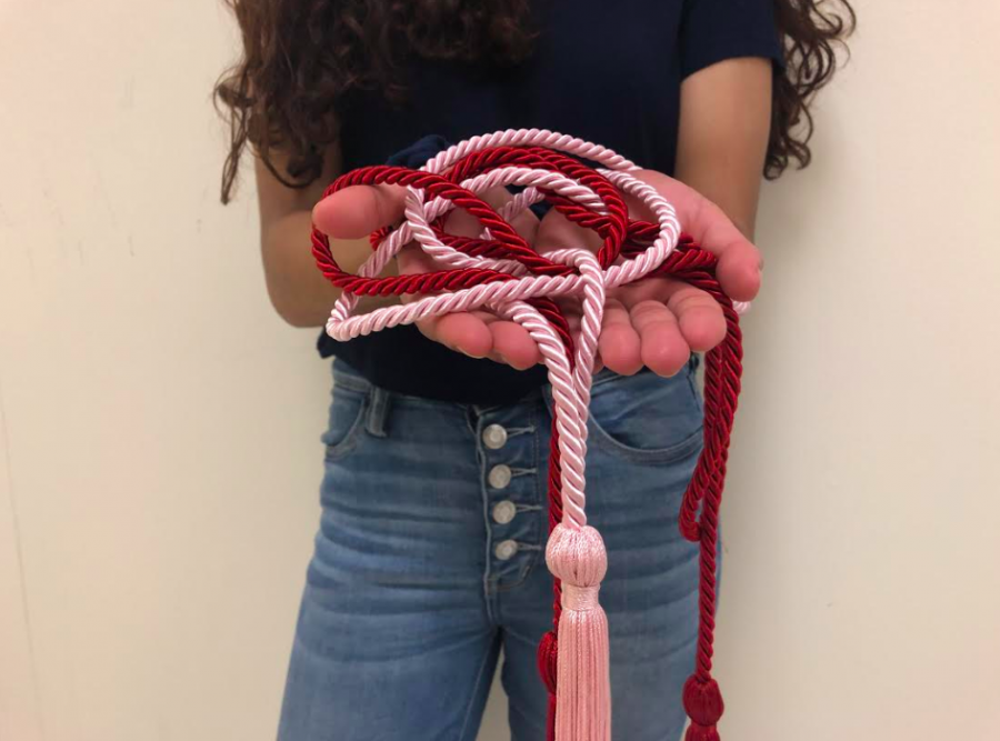 A 2018 graduate holds cords from Tri-M and Interact. Due to the new graduation cord policy, many cords are being cut this year in an effort to limit the number of students at senior honors night. 