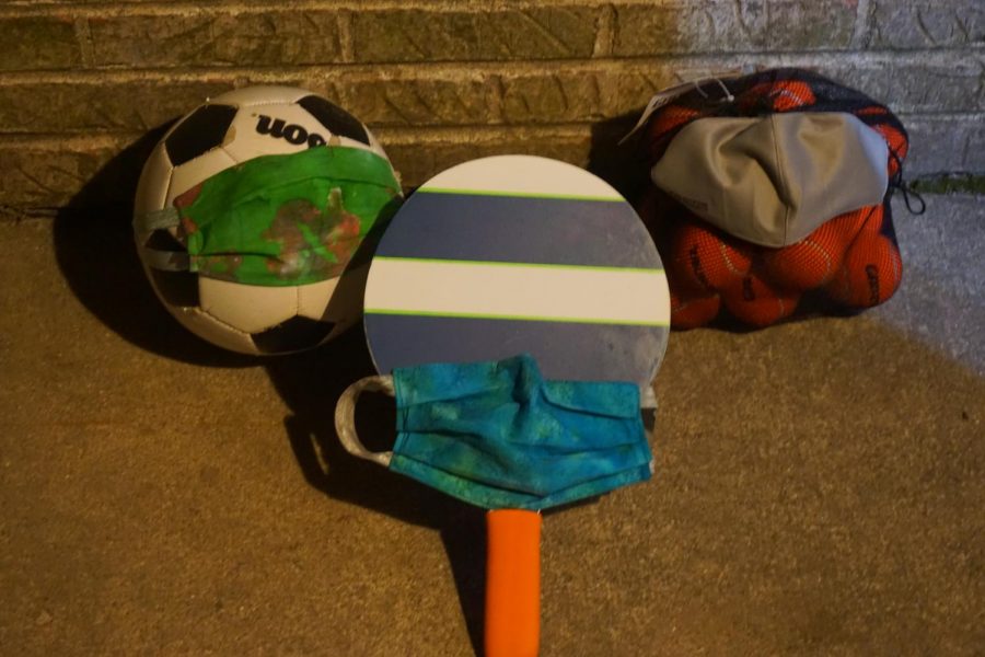 A soccer ball, ping-pong paddle, and a bag of tennis balls lay on the ground. This equipment cannot be used for PE classes due to curriculum changing to low-intensity workouts and mindfulness.