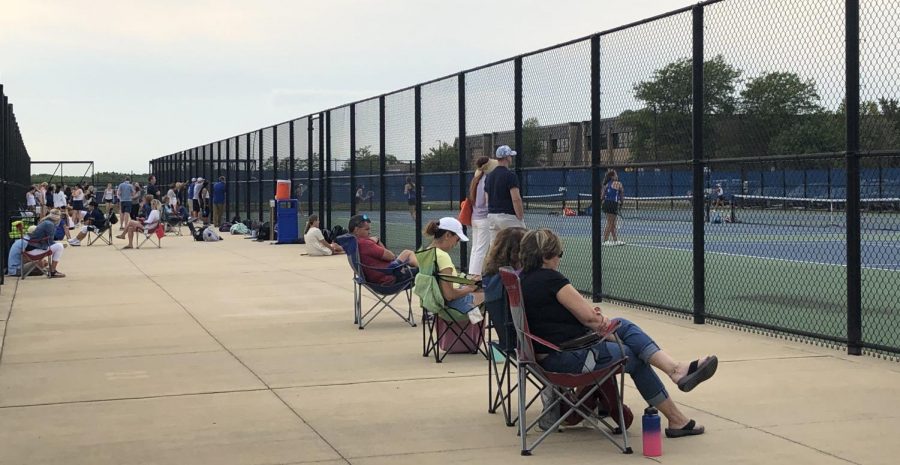 Family members of tennis players sit beside the courts to cheer on their children. 
