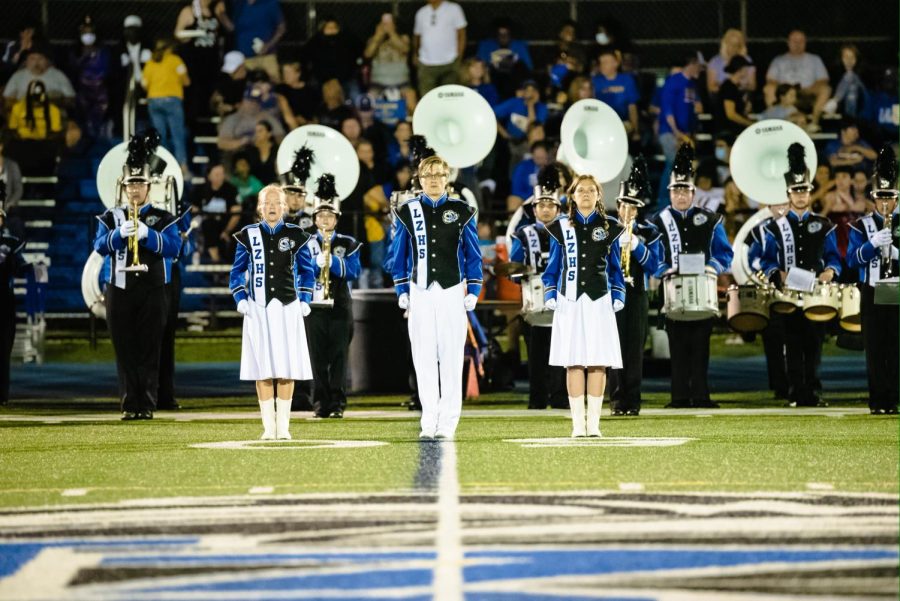 (From left to right) Kate Thompson, David Appel, and Natalie Dziubinski stand in front of the performing marching band during a football game.