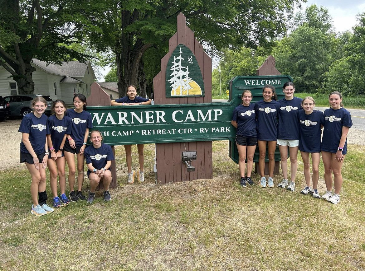 After+a+week+of+training+in+Michigan%2C+Summer+Fabsik+%28pictured+fifth+from+the+right%29+poses+with+some+of+the+distance+runners+in+front+of+the+summer+camp+sign.