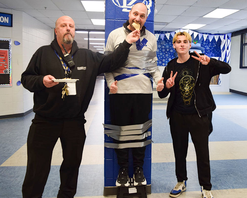 Ron Planz, PE teacher, being taped to the wall with a student and a security guard. This was during Planz lunch period, so it was important he ate.